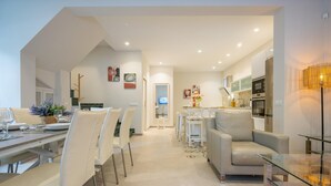 A modern interior with a dining area, a sofa, a kitchen, and a TV in the background.