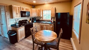 A kitchen with wooden cabinets, a stove, a microwave, a refrigerator, and a dining table with chairs. - Brand New! Bright, Airy Cabin Boarding Winslow Hill Elk Viewing Area! (Benezette)