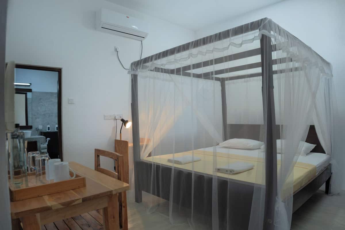 A room with a four-poster bed, a wooden desk, a mirror, and an air conditioning unit.