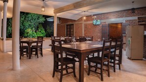 An outdoor dining area with brick walls, wooden tables and chairs, and a large window overlooking greenery. - Wild Edge Panama - Kumana Safari Lodge (Panama)