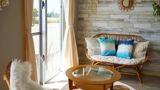 A room with a wicker sofa, a glass coffee table, and a white fluffy chair.