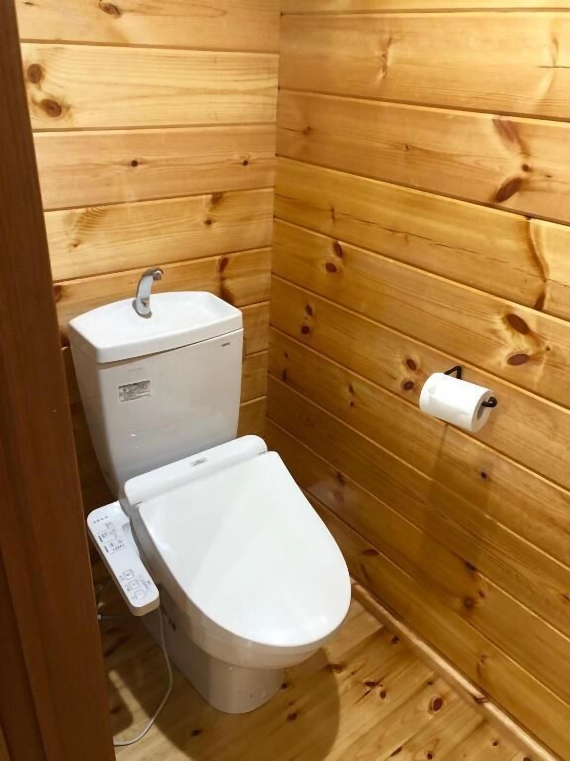 Une petite salle de bain aux murs lambrissés, équipée de toilettes, d’un porte-rouleau de papier toilette et d’un panneau de commande.