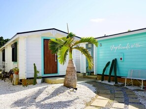 A building with a white exterior and a turquoise door, a palm tree in the center, and a bench to the right. - Guest house KAZE (Miyakojima)