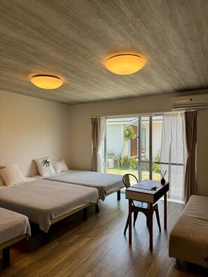Una habitación con dos camas, una mesa y una silla. Hay una ventana con cortinas y un equipo de aire acondicionado en la pared.