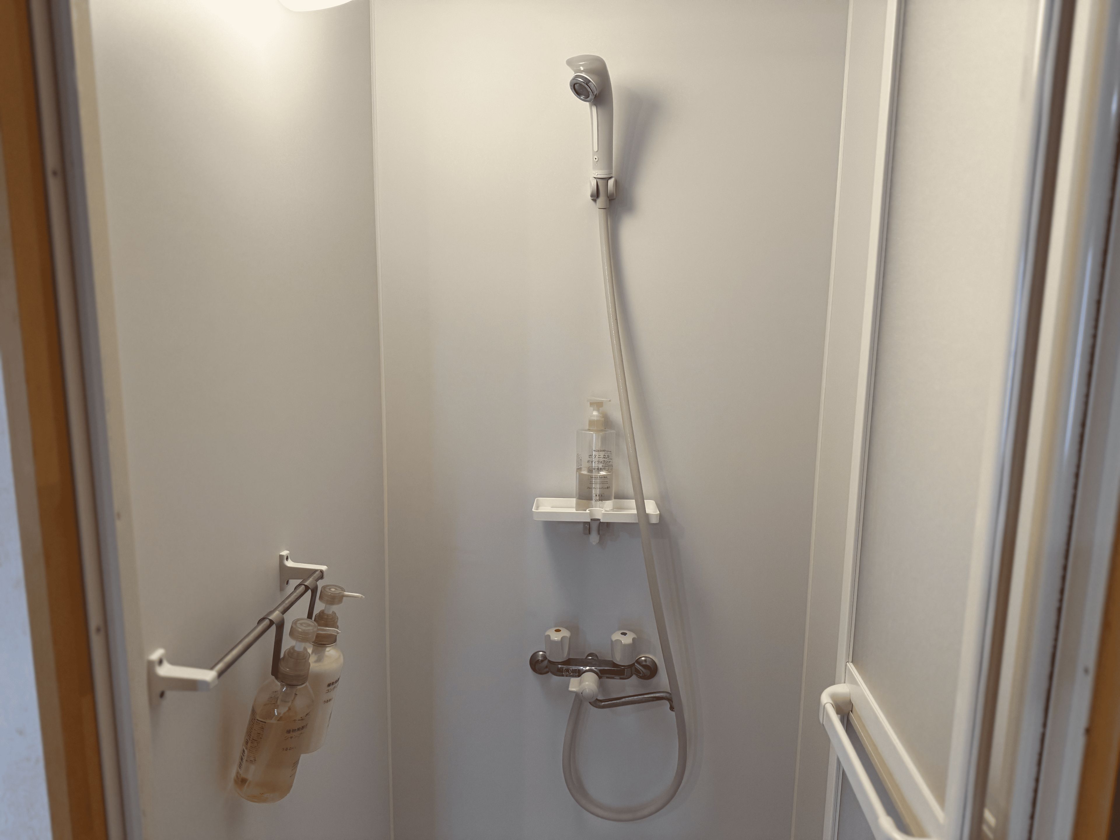 En dusch med ett duschhuvud som kan hållas i handen, en väggmonterad blandare och en tvåldispenser.