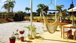 A covered outdoor seating area with a hammock, potted plants, and a table with chairs.