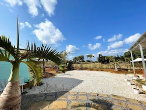 A gravel patio with potted plants, a palm tree, and a clear blue sky. - Guest house KAZE (Miyakojima)