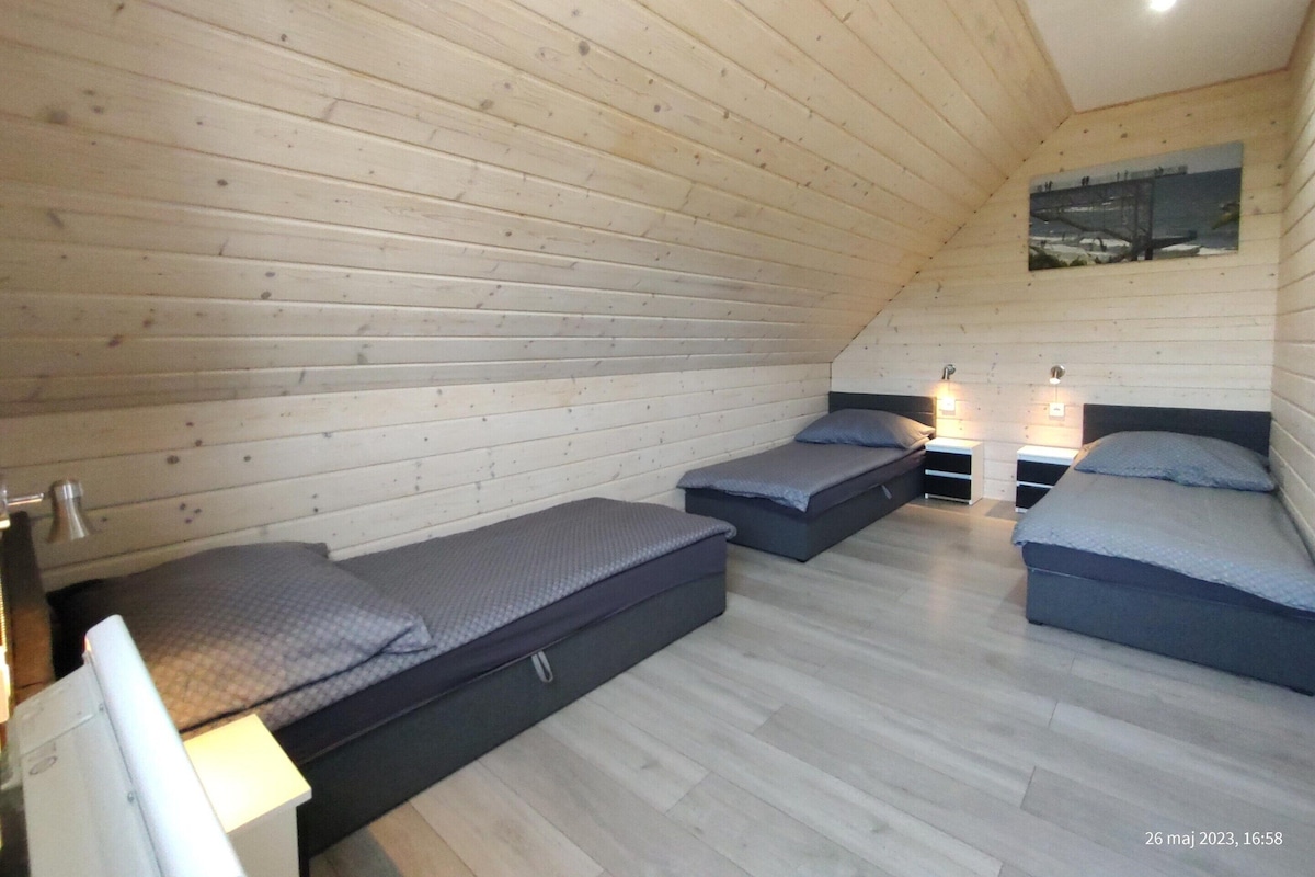 A room with wooden walls, two beds, a small table, and a painting on the wall.