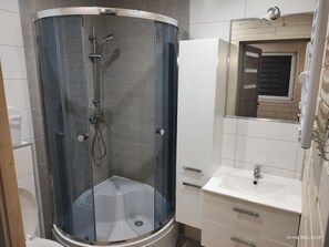 Ein modernes Badezimmer mit einer gläsernen Duschkabine, einem weißen Waschbecken und einem Spiegel darüber.