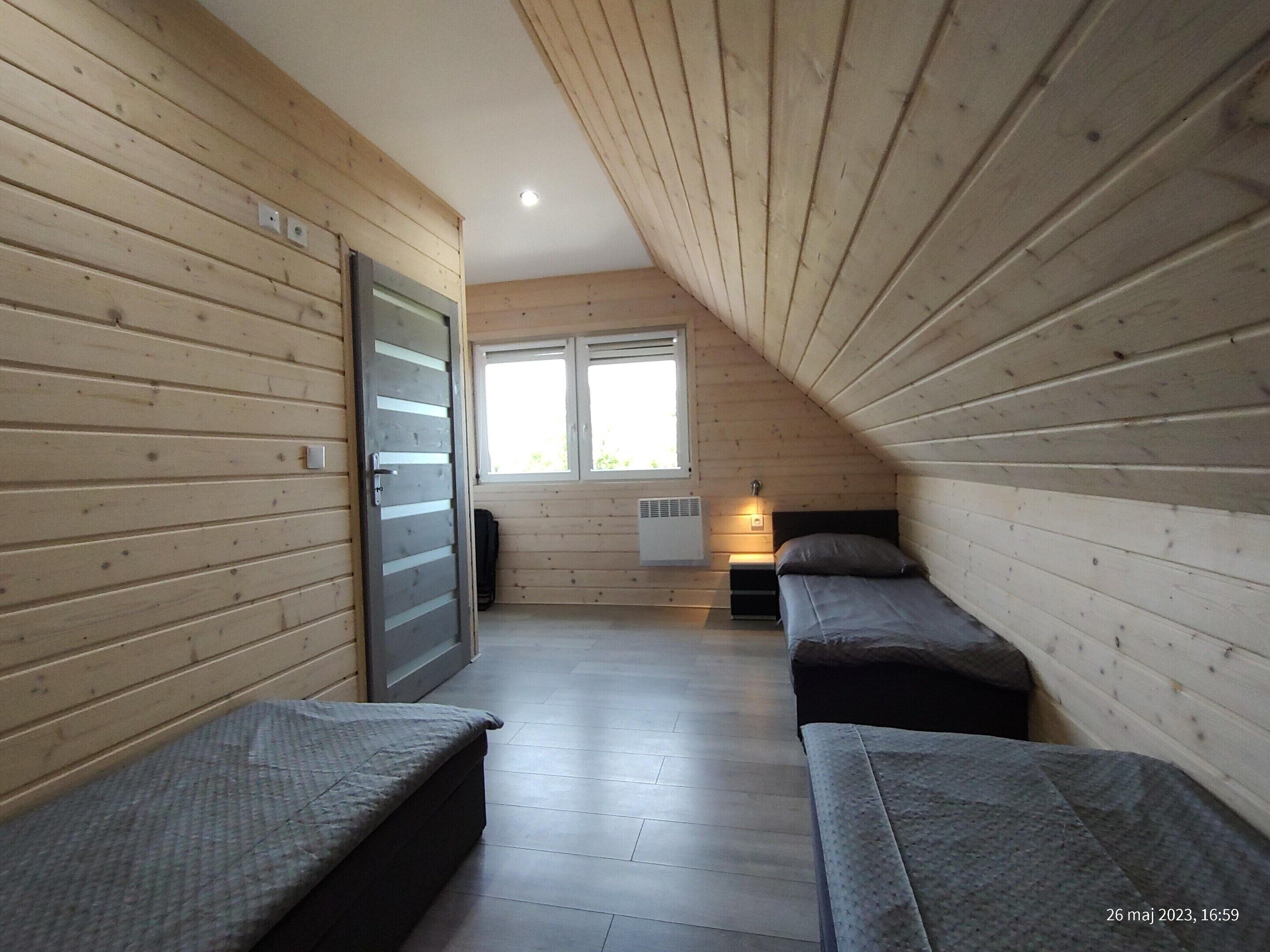 A room with wooden walls, a sloped ceiling, a bed, a bedside table, a window, and a radiator.