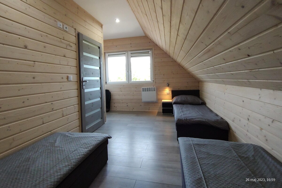 A room with wooden walls, a sloped ceiling, a bed, a bedside table, a window, and a radiator.
