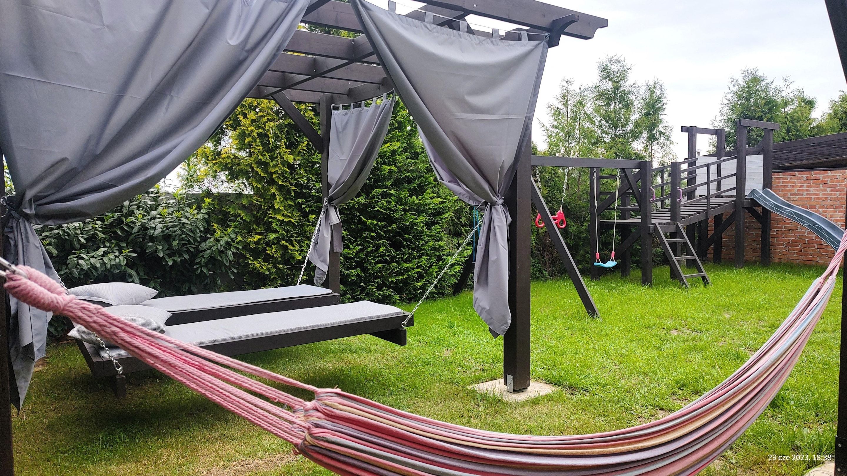 A hammock under a pergola with a slide and stairs in the background.