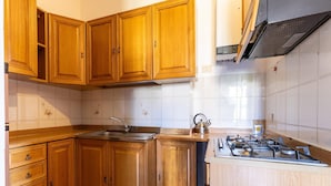 Een keuken met houten kastjes, een roestvrijstalen spoelbak, een waterkoker en een gasfornuis.