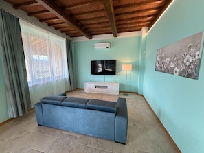 Ein Wohnzimmer mit einem blauen Sofa, einem Flachbildfernseher, einer Stehlampe und einem Gemälde an der Wand.