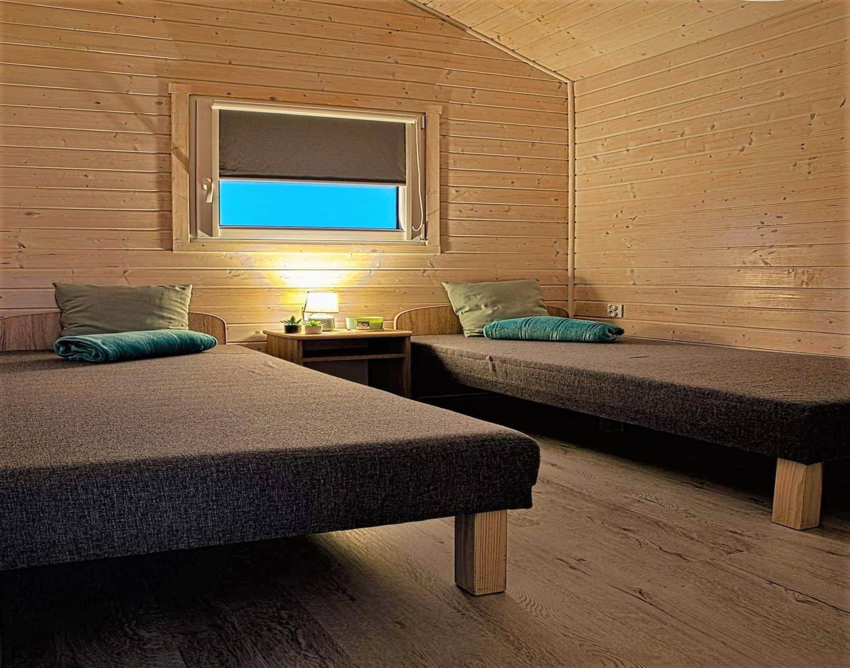 Eine Hütte mit zwei Betten, einem Nachttisch, einer Lampe und einem Fenster mit Blick.