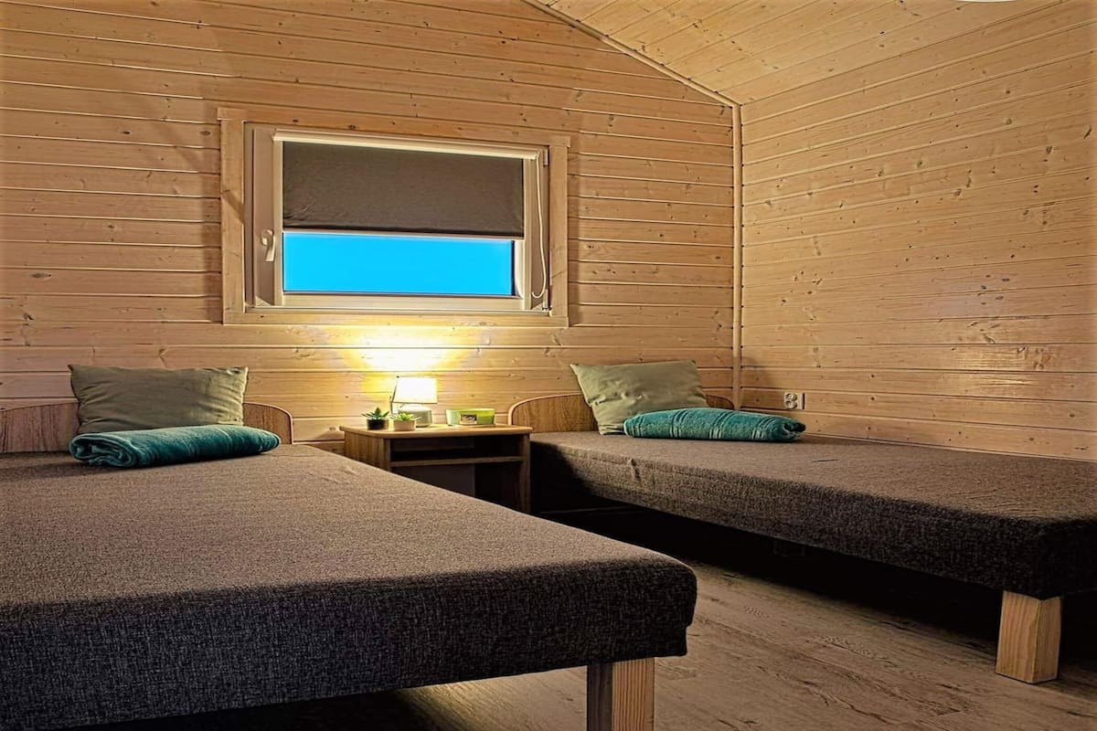 Una cabaña con dos camas, una mesita de noche, una lámpara y una ventana con vistas.