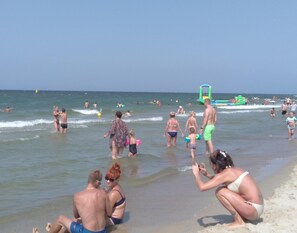 A beach scene with people swimming and playing, a green inflatable structure, and a clear sky.