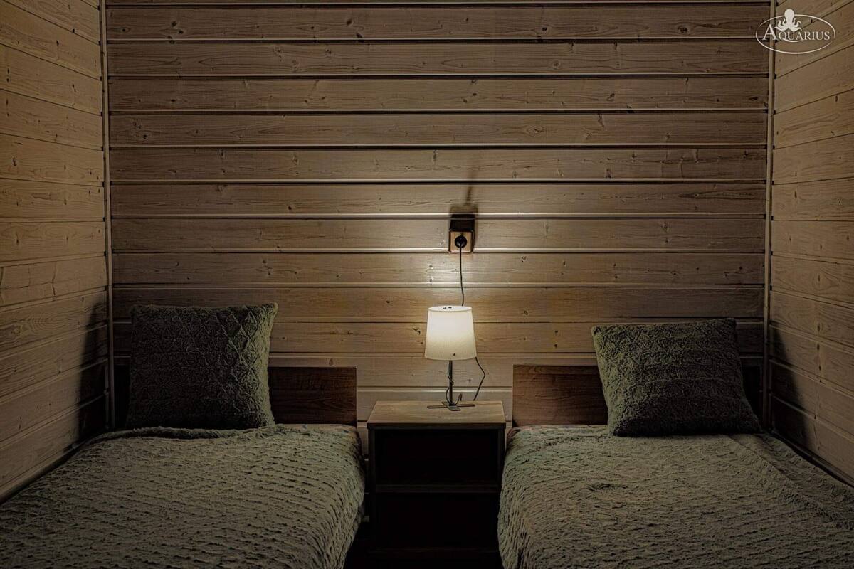 Una habitación acogedora con paredes de madera, dos camas con almohadas a juego y una mesita de noche con lámpara.