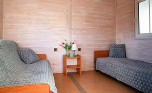 Ein kleiner, gemütlicher Raum mit zwei Einzelbetten, einem Holznachttisch mit Lampe und Blumen, sowie einem Fenster.