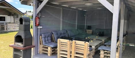 Un espace extérieur abrité avec un barbecue, des sièges rembourrés et un extincteur.