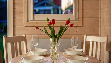 A wooden dining table with white plates and empty wine glasses, a vase with red tulips, and a window with a view of buildings.