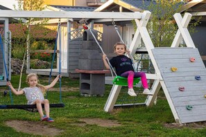 Two children on swings in a backyard with a climbing wall and a playhouse. - Holiday Home in Dziwnowek by Baltic Sea (Kamien Pomorski)
