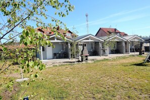 A row of small, single-story houses with numbered doors, a barbecue grill, and a clear sky.