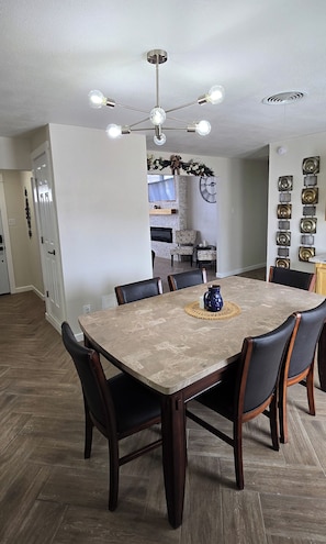 A dining area with a marble table, dark wooden chairs, a chandelier, and a decorative wall piece.
