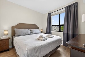 A hotel room with a bed, bedside tables, a desk, and a window with curtains. - Two bedroom  in Canada, Kelowna (Kelowna)