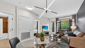 Een moderne woonkamer met een glazen eettafel, lederen fauteuils, een bank en een televisie.