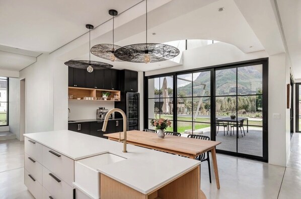 A modern kitchen with a large island, black cabinets, and a view of a mountain landscape through large sliding doors.