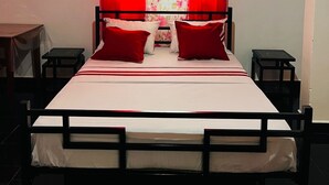 A bed with a headboard, red curtains, and a floral window treatment. - Apartment no. 5 (Antsiranana)