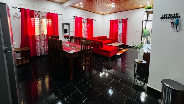 A modern living room with a dining area, red curtains, a red sofa, and a 'HOME' sign on the wall. - Apartment no. 5 (Antsiranana)