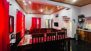 A dining area with a wooden table and chairs, red curtains, a television, and a kitchen area with a microwave. - Apartment no. 5 (Antsiranana)