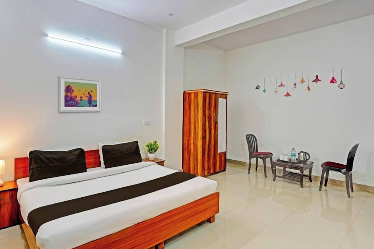 A hotel room with a bed, bedside table, lamp, chair, small table, and a wardrobe.
