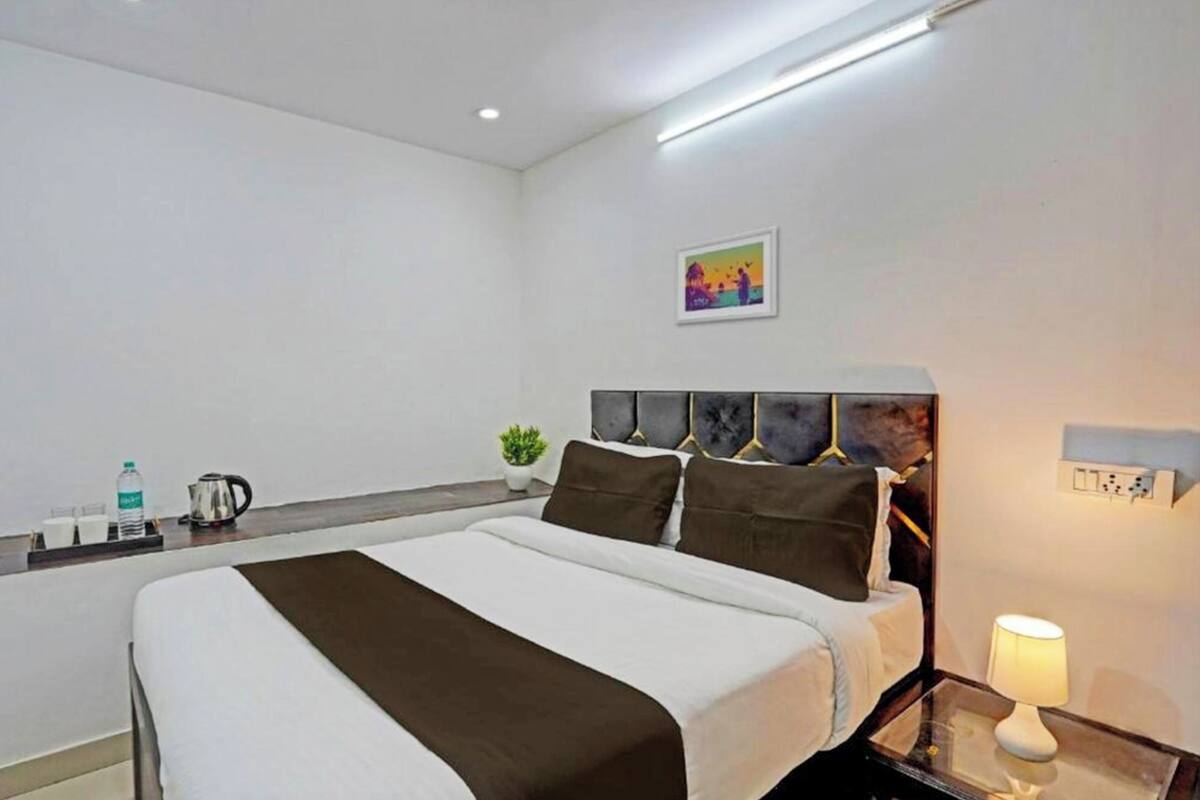 A modern hotel room with a large bed, bedside tables, a nightstand, a lamp, a painting on the wall, and a small potted plant.