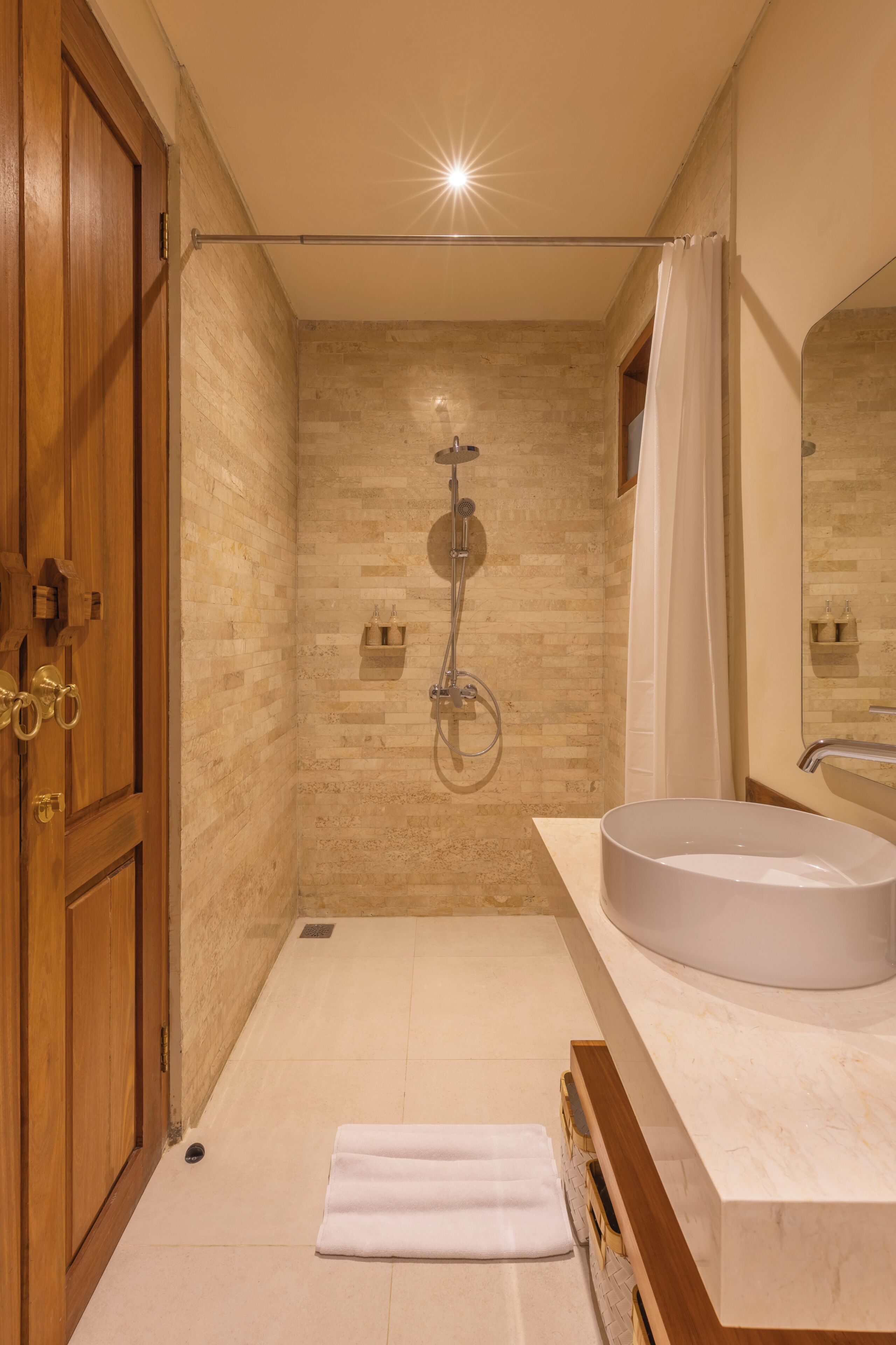 A modern bathroom with a shower, a sink, and a wooden door.