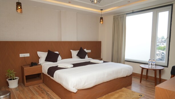 Ein Hotelzimmer mit einem großen Bett, Nachttischen, einem Topf mit Pflanze, einem Schreibtisch und einem Fenster mit Aussicht.