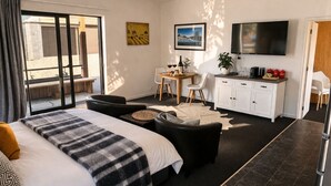 Moderni hotellihuone, jossa on suuri sänky, sohva, ruokailutila, televisio ja parveke.