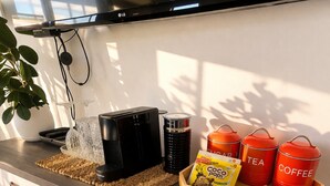 Keittiön työtasolla on kahvinkeitin, vedenkeitin, kahvipapujen säiliö ja pakkaus kahvikapseleita.