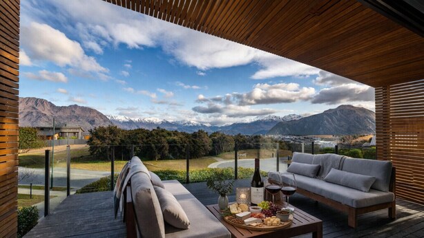 Eine Holzterrasse mit einer Couch und einem Tisch, gedeckt für eine Mahlzeit, mit Blick auf eine gebirgige Landschaft.