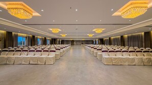 A large conference room with rows of chairs, chandeliers, and a long table at the front. - Jain Tree by Spree Hotels Vellore (Katpadi)