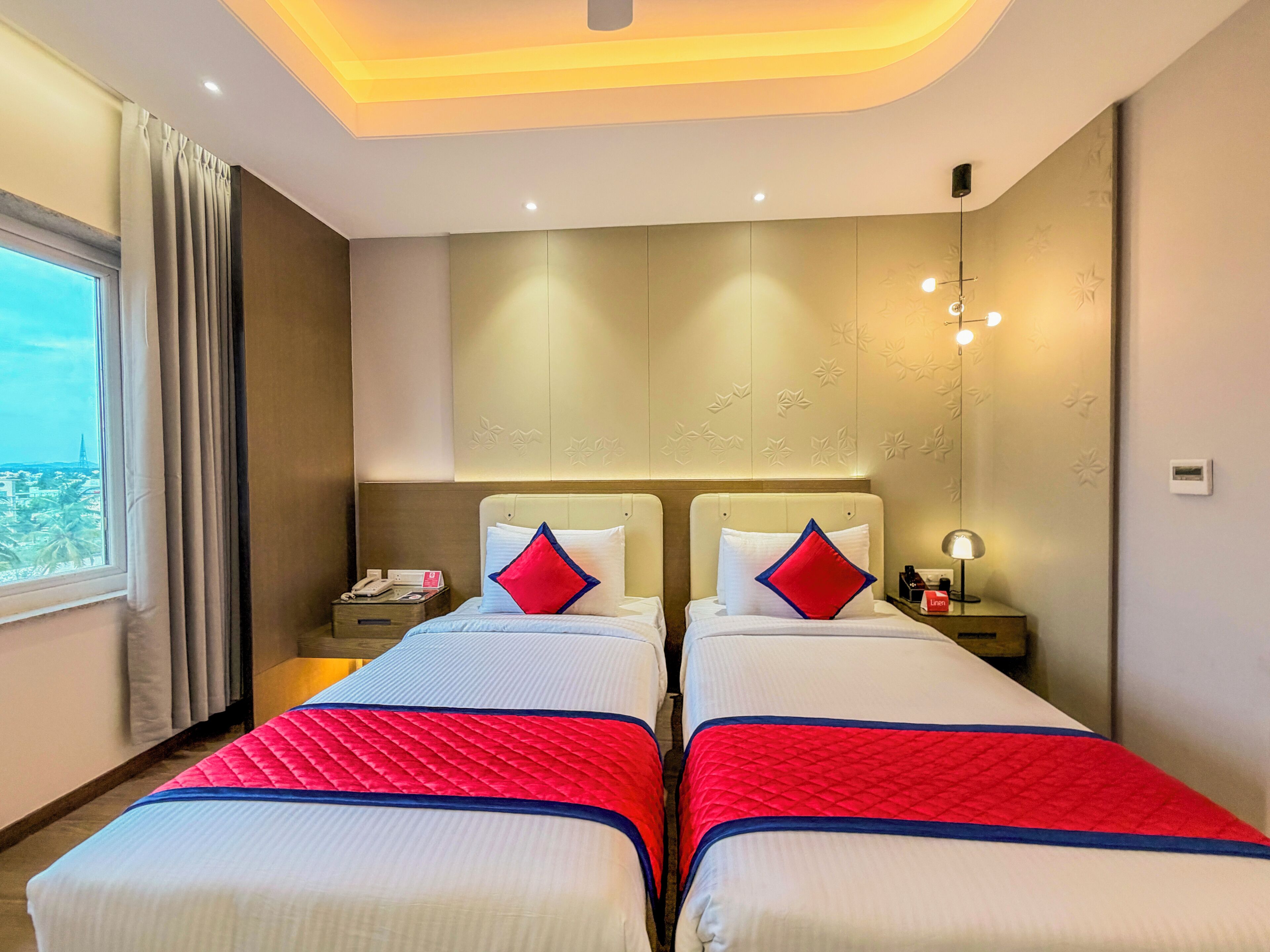 Een hotelkamer met twee bedden, een nachtkastje met telefoon, lamp en een raam met gordijnen.