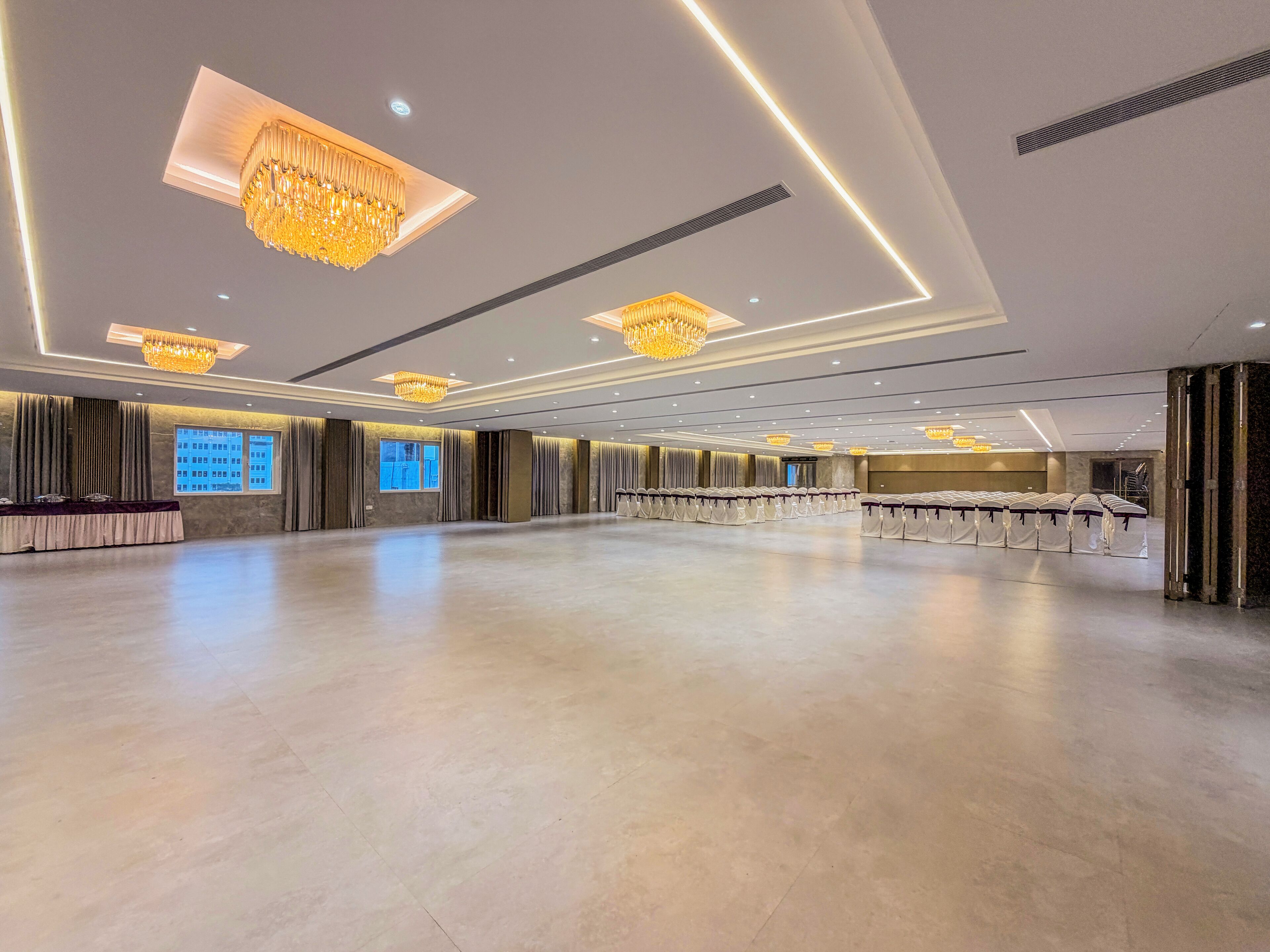 A spacious hall with a long table set for a banquet, large chandeliers, and a modern ceiling design.