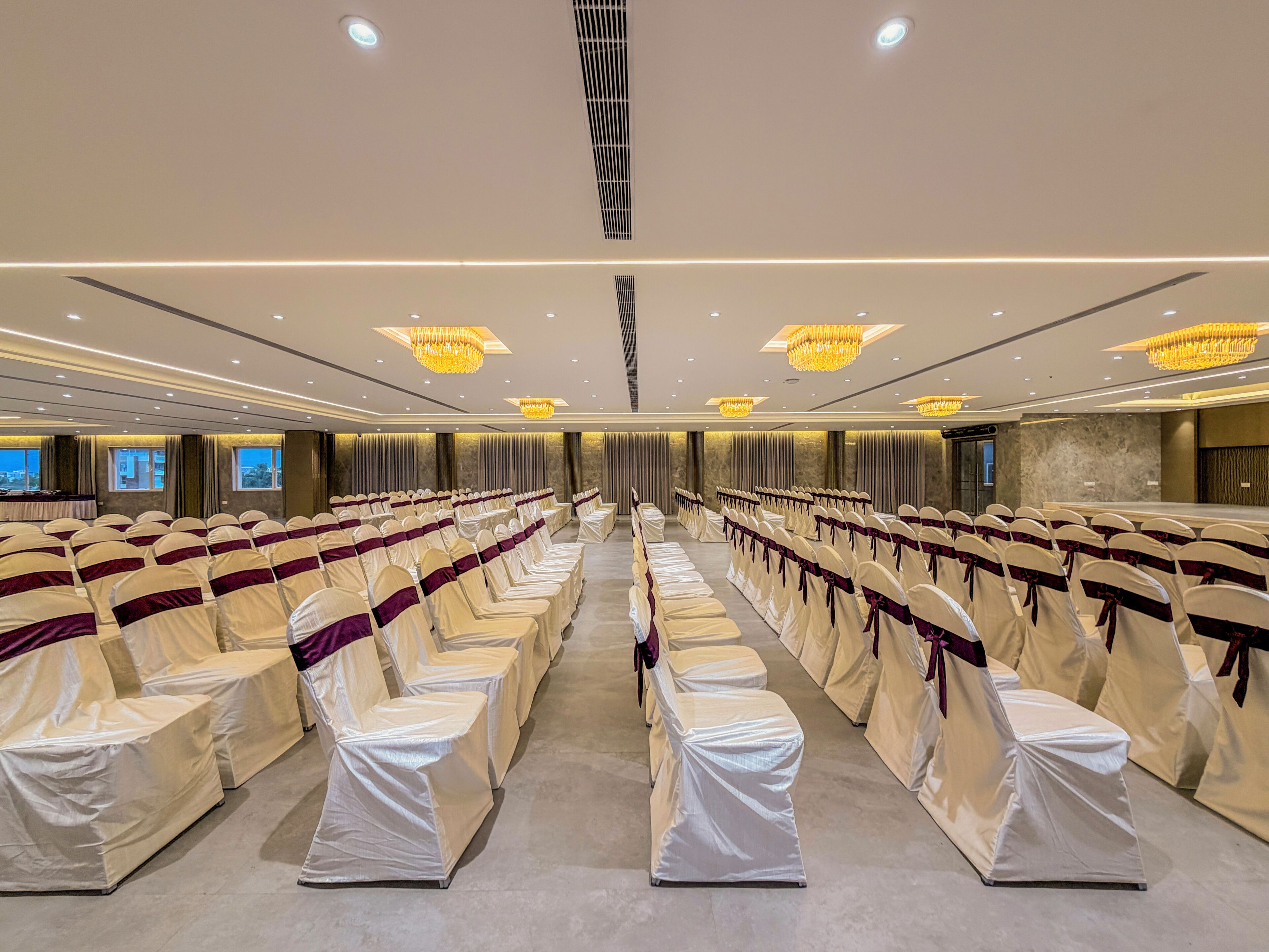 A conference room with rows of chairs, a stage, and chandeliers.
