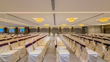 A conference room with rows of chairs, a stage, and chandeliers.