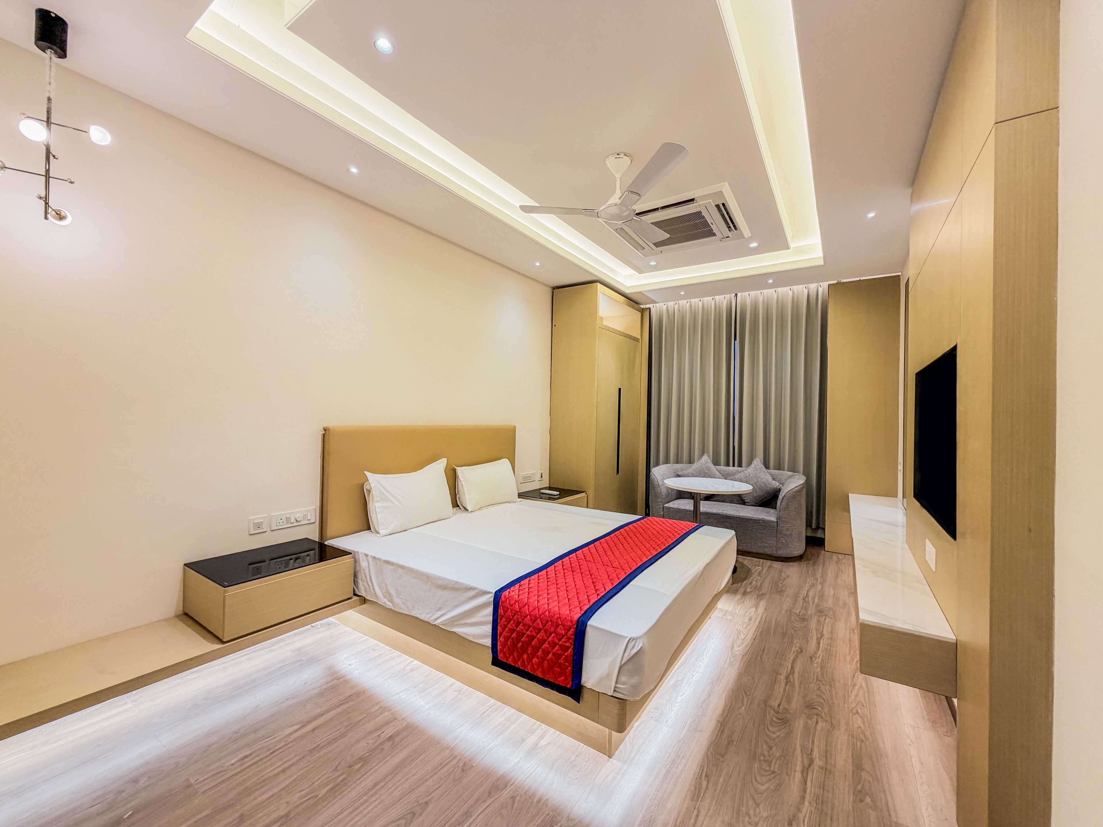 A modern hotel room with a bed, bedside table, and a seating area with curtains.