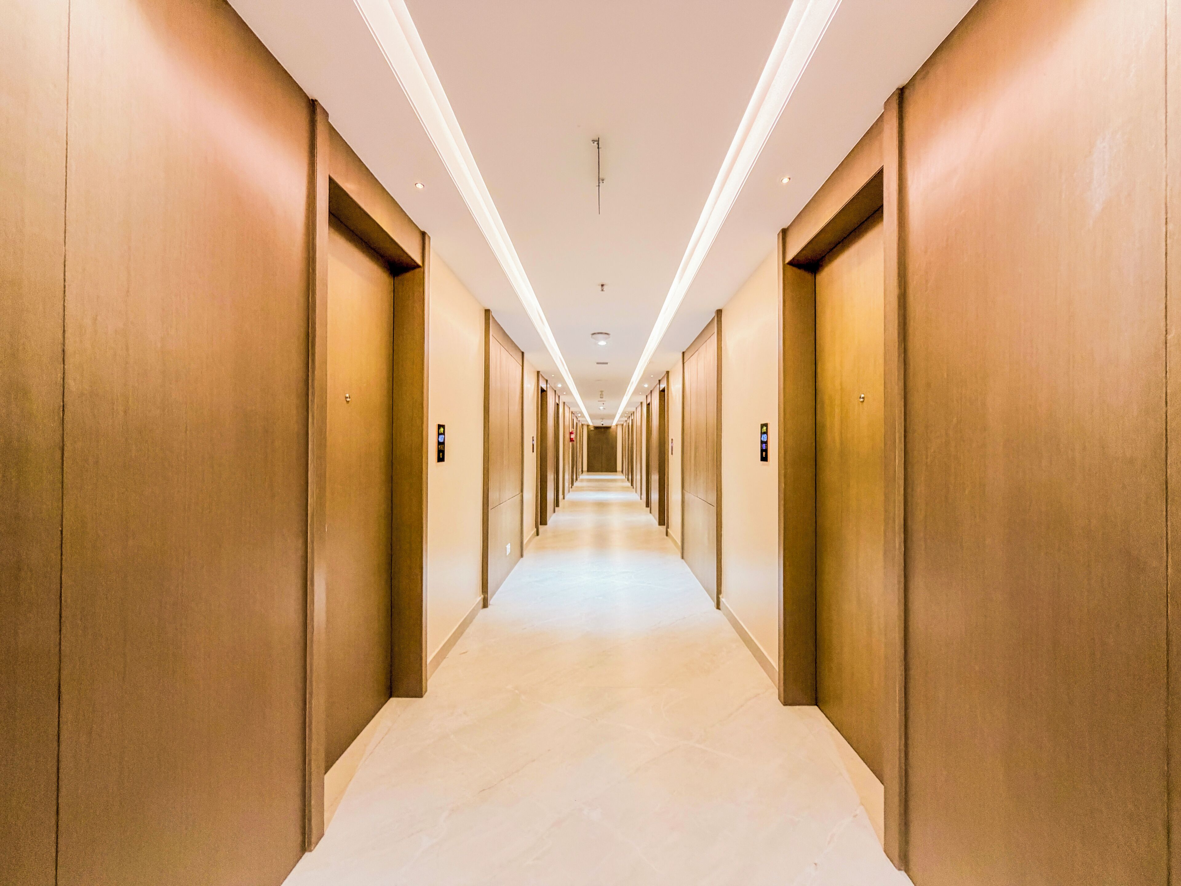 Un largo y estrecho pasillo de hotel con puertas a ambos lados, piso de color claro e iluminación empotrada en el techo.