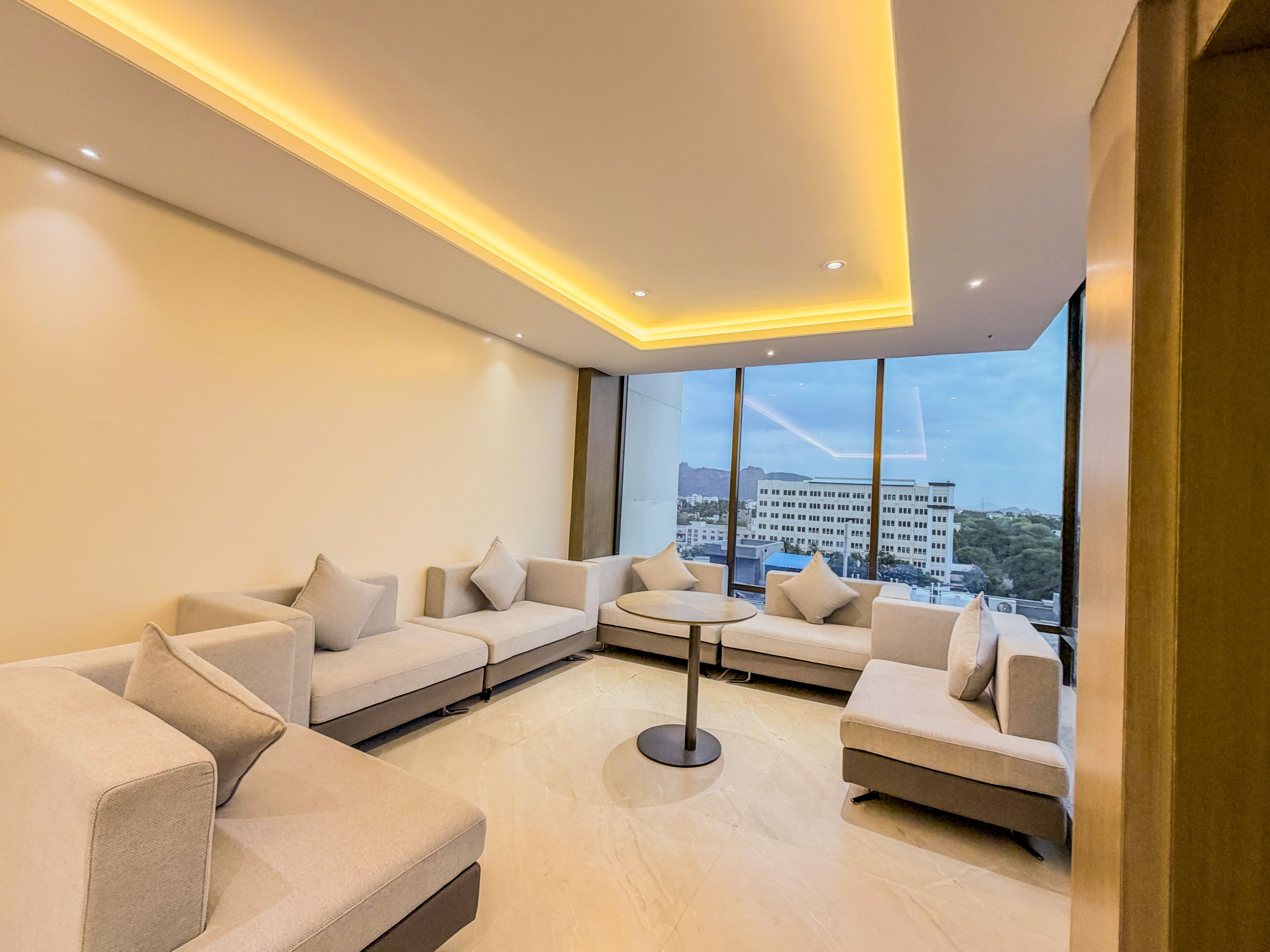 A modern living room with a sectional sofa, a round coffee table, and large windows offering a city view.