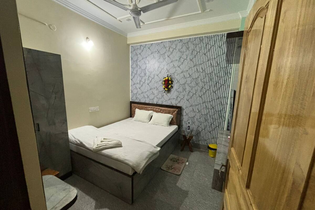 A bedroom with a bed, a ceiling fan, a small table, a wall-mounted light, and a door.